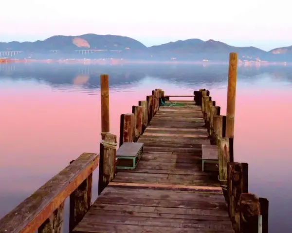 Pontile in legno su lago calmo al tramonto, con montagne sullo sfondo. Si intuisce dove si trova Torre del Lago.
