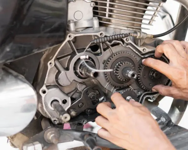 Mani che lavorano sul motore di una moto, forse per risolvere una perdita di potenza auto benzina. Ingranaggi e parti meccaniche in vista.