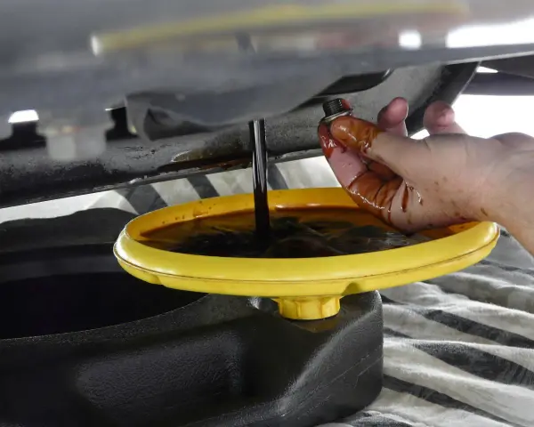 Cambio olio: un tappo sporco di olio viene tenuto da una mano mentre l'olio esausto cola in un contenitore. Forse c'era troppo olio nel motore.