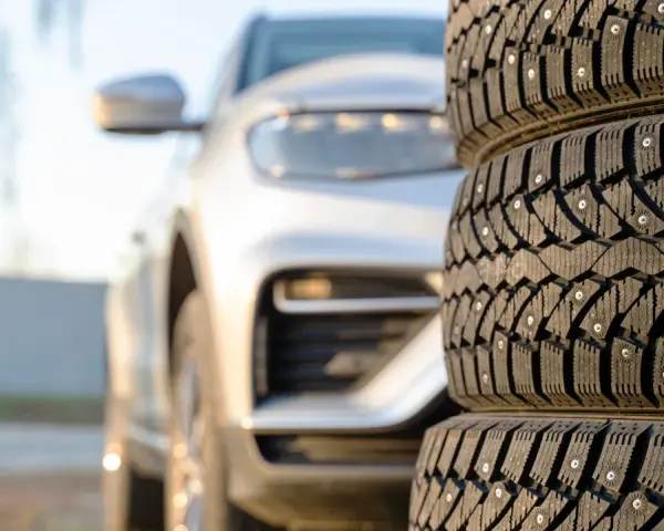 Gomme invernali con chiodi in primo piano, un'auto bianca sfocata sullo sfondo. Preparazione per l'inverno, anche se è estate.