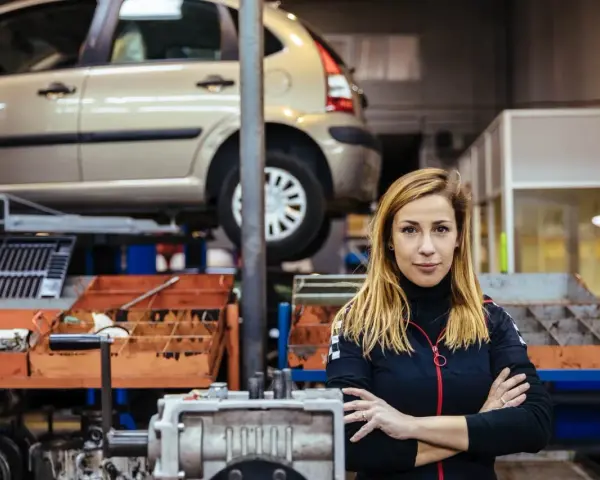 Donna in officina con auto sollevata, pronta per la manutenzione straordinaria auto.
