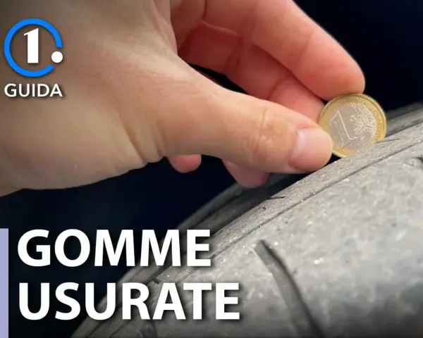 Una mano controlla l'usura di un pneumatico con una moneta da 1 euro. La tela del pneumatico è visibile, mostrando quanto sia consumata.