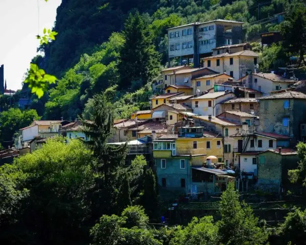 Case colorate e tetti rossi si aggrappano alla collina a Casoli di Camaiore, circondate da un verde lussureggiante.