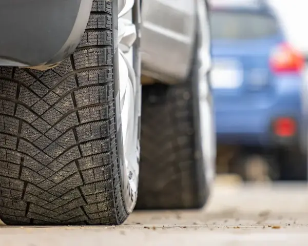 Primo piano di pneumatici invernali, con un'altra auto in lontananza. La classe rumorosità pneumatici è un fattore importante per il comfort di guida.