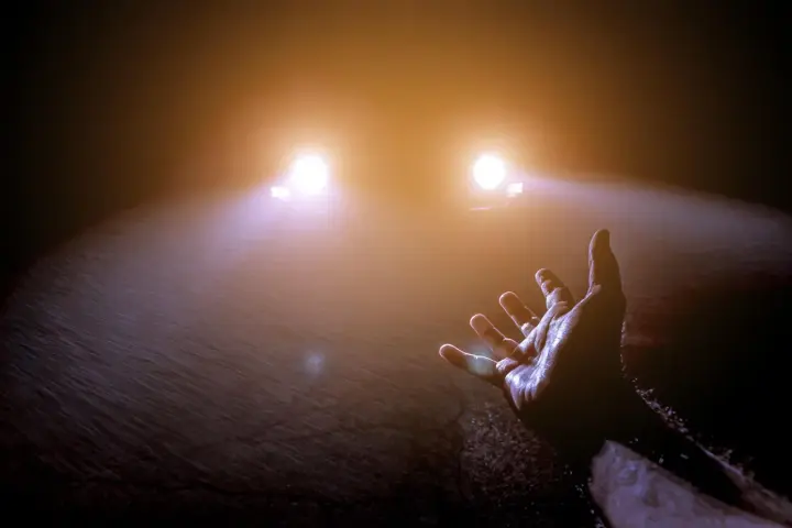 Mano tesa verso le luci abbaglianti di un'auto nella nebbia, un momento di incertezza e speranza.