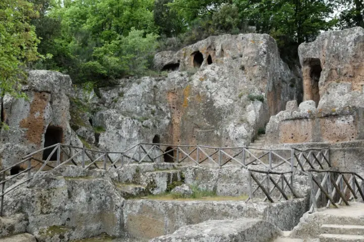 Antiche tombe scavate nella roccia, parte dei siti etruschi in Toscana, con sentieri e recinzioni in legno.