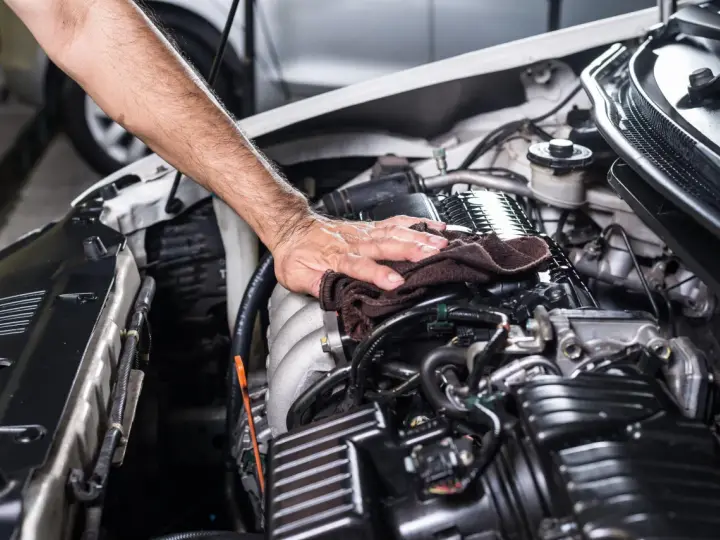 Mano che pulisce il motore dell'auto con un panno. Non è consigliabile usare l'idropulitrice per lavare il motore della macchina.