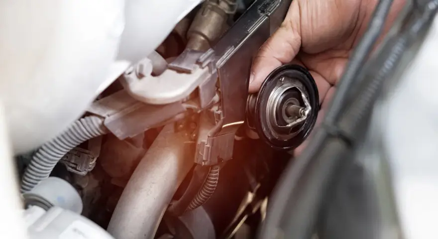 Mano che rimuove il termostato dell'auto. Un bulbo radiatore rotto può causare surriscaldamento.