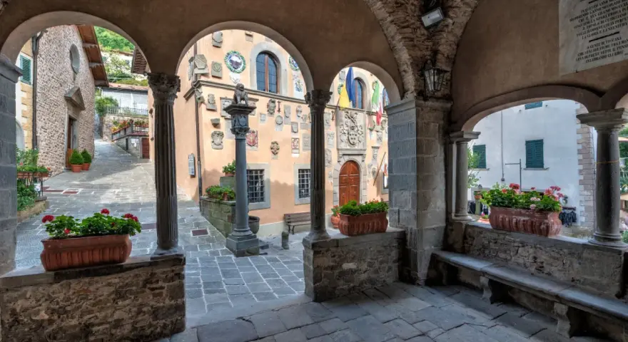 Un vicolo tra i borghi della montagna pistoiese, con archi in pietra, colonne e vasi di fiori rossi.