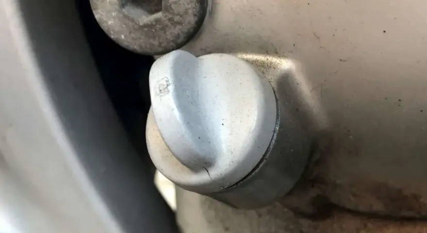 Dettaglio di un tappo motore con una piccola crepa, suggerendo una possibile fuoriuscita olio motore dal tappo.