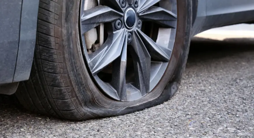 Ruota dell'auto con pneumatico sgonfio, mostra un'ernia evidente. Un problema comune che richiede attenzione immediata.