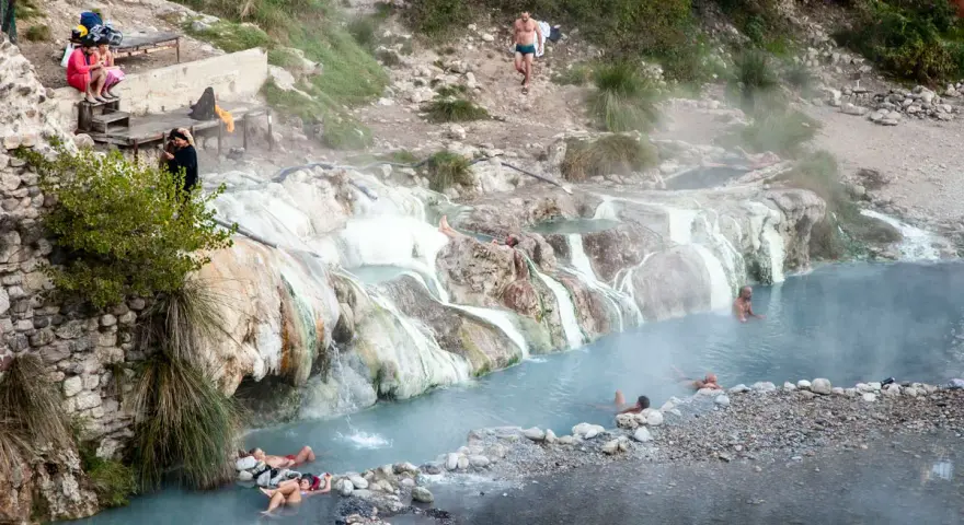 Persone si rilassano nelle calde acque delle terme di Petriolo libere, tra rocce e vegetazione.