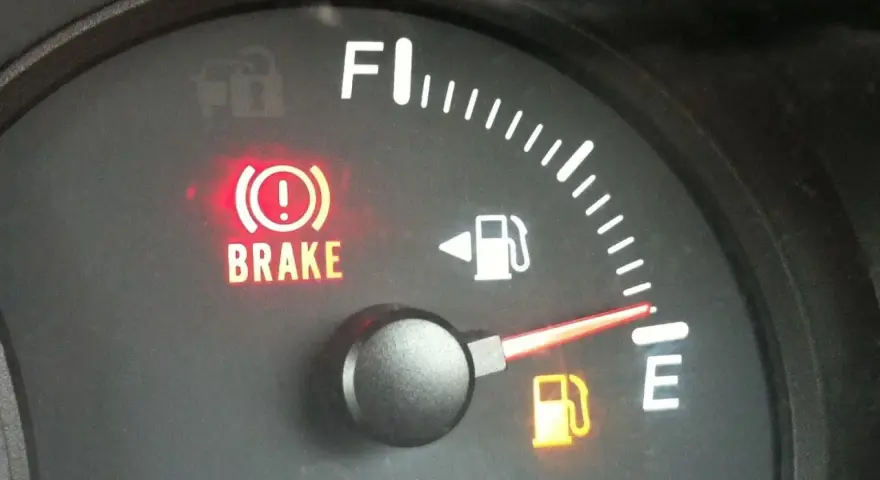 Cruscotto auto con spia freno a mano accesa e indicatore carburante quasi vuoto. È ora di fare rifornimento e resettare l'indicatore carburante.