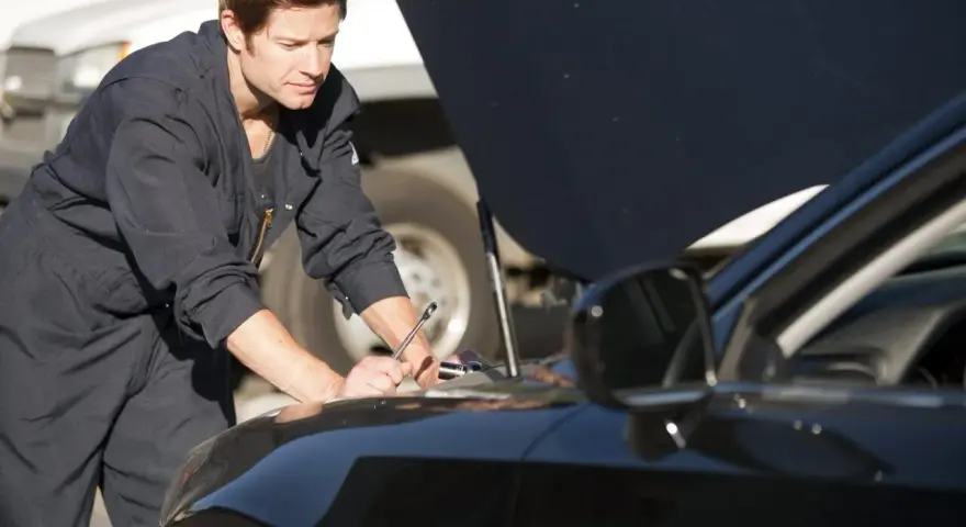 Meccanico in tuta blu lavora sul motore di un'auto nera. La revisione auto si può fare in tutta Italia, ovunque ci sia un professionista.