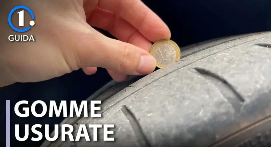 Una mano inserisce una moneta da 1 euro in un pneumatico usurato, indicando che è consigliabile sostituire gli pneumatici per la sicurezza.
