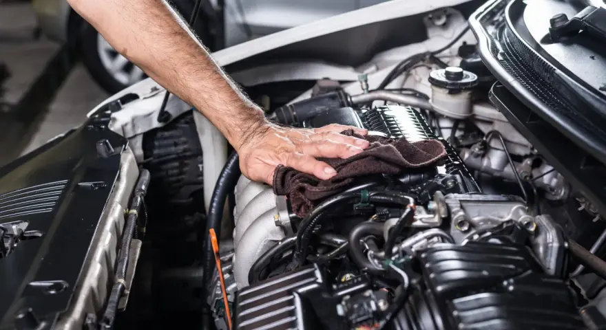Mano che pulisce il motore dell'auto con un panno. Non è consigliabile usare l'idropulitrice per lavare il motore della macchina.
