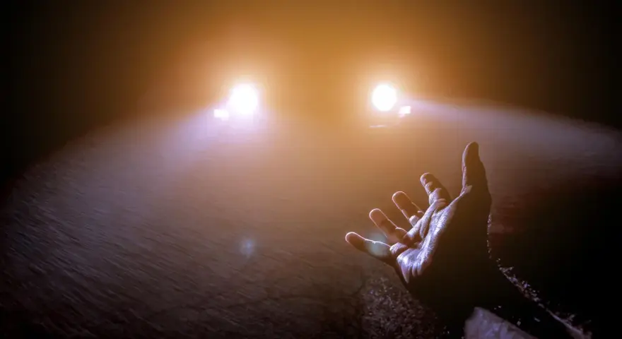 Mano tesa verso le luci abbaglianti di un'auto nella nebbia, un momento di incertezza e speranza.