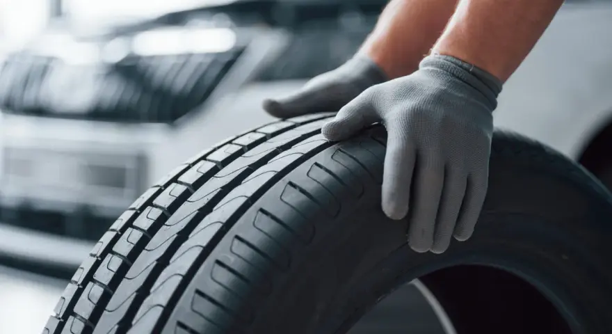 Mani guantate controllano il battistrada di uno pneumatico, valutando la sua durata gomme auto.