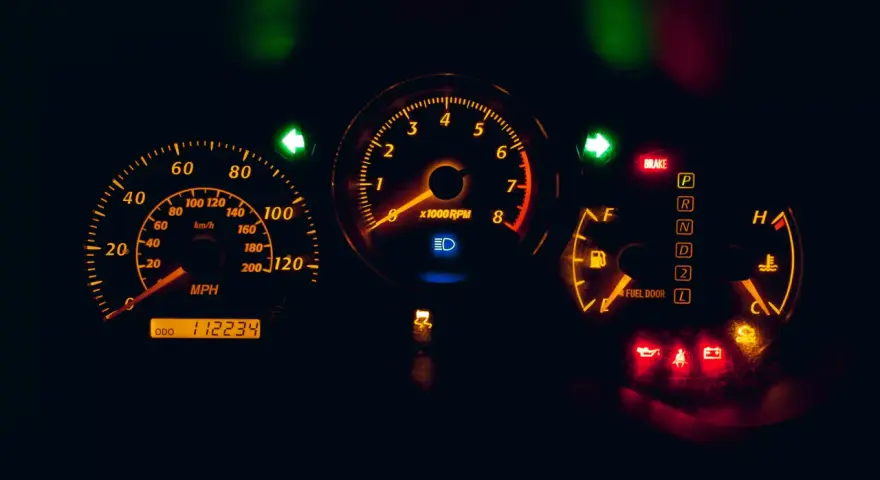 Cruscotto auto illuminato di arancione: tachimetro, contagiri, indicatori di marcia e spie accese, tra cui una spia arancione macchina.