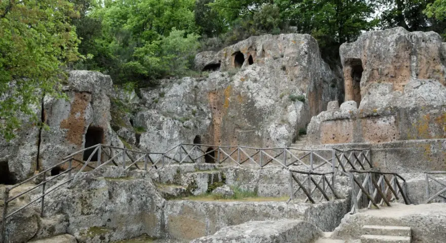 Antiche tombe scavate nella roccia, parte dei siti etruschi in Toscana, con sentieri e recinzioni in legno.
