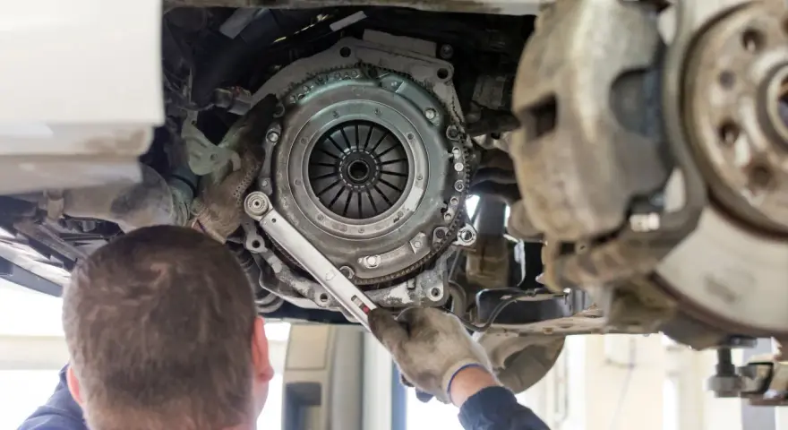 Meccanico lavora sulla frizione di un'auto. La durata della frizione varia, ma si consiglia di controllarla ogni quanti km si cambia la frizione.