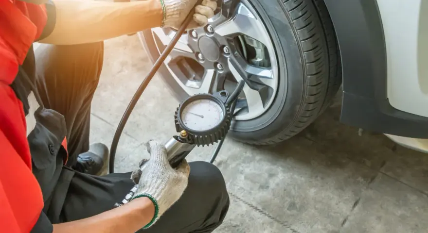 Controllo pressione gomme a caldo o freddo con manometro. Un meccanico in tuta rossa verifica la pressione degli pneumatici.