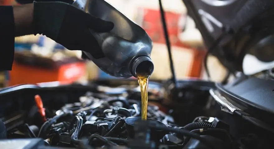 Mano con guanto versa olio motore. Il cambio olio ogni quanto è fondamentale per la salute dell'auto.