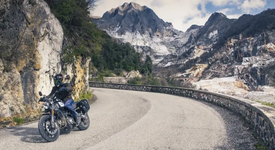 Un motociclista percorre una strada tortuosa tra le cave di marmo delle Alpi Apuane, un'avventura tra i passi toscana moto.