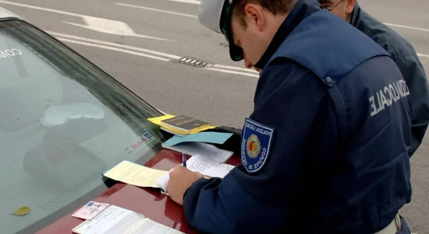 Agente di polizia scrive verbale su un'auto con revisione scaduta da 2 anni. Documenti e patente sul cofano.
