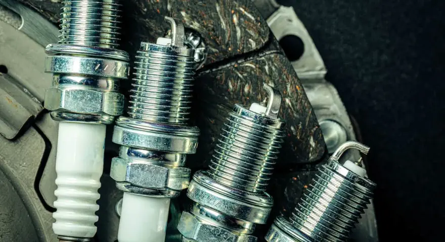 Candele auto benzina: scopri ogni quanto cambiarle per un motore efficiente. Nuove candele in primo piano su uno sfondo scuro.