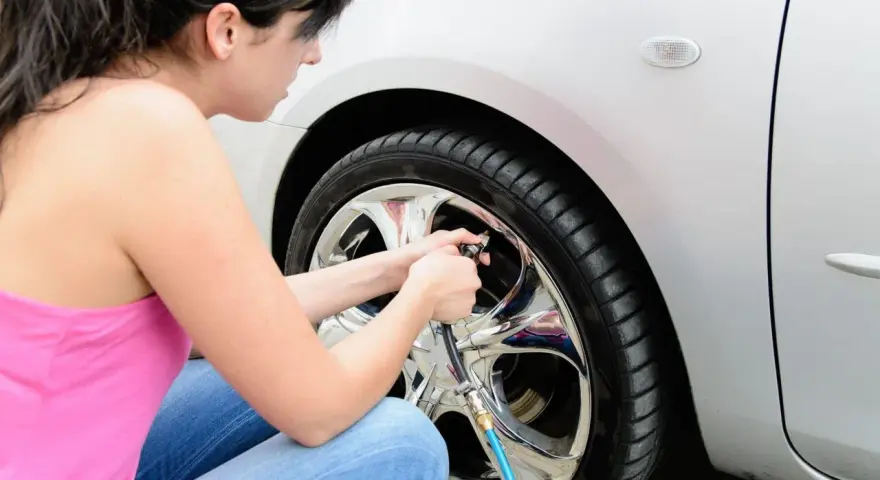 Donna controlla la pressione gomme auto estate, assicurandosi che siano gonfie al punto giusto per un viaggio sicuro.