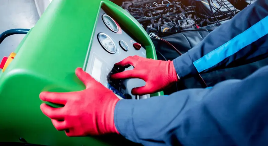 Tecnico con guanti rossi usa una macchina per controllare la perdita gas condizionatore auto.