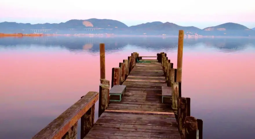 Pontile in legno su lago calmo al tramonto, con montagne sullo sfondo. Si intuisce dove si trova Torre del Lago.