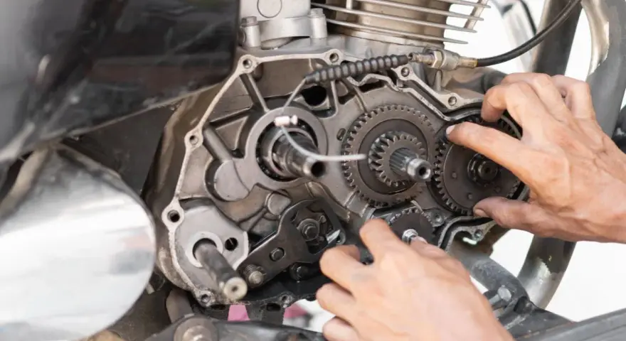Mani che lavorano sul motore di una moto, forse per risolvere una perdita di potenza auto benzina. Ingranaggi e parti meccaniche in vista.