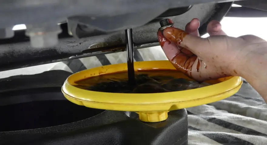 Cambio olio: un tappo sporco di olio viene tenuto da una mano mentre l'olio esausto cola in un contenitore. Forse c'era troppo olio nel motore.
