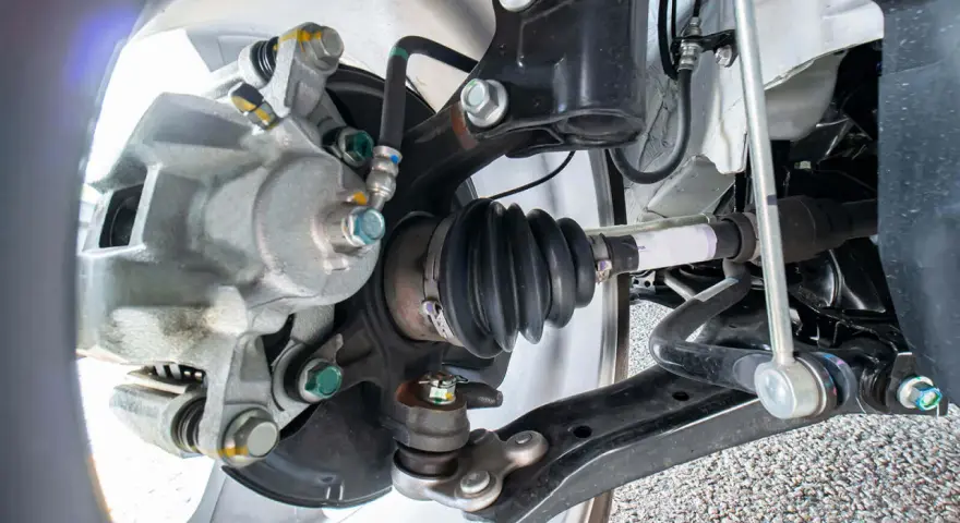 Parti della sospensione di un'auto, inclusa la pinza del freno e il giunto omocinetico con soffietto, utili per riconoscere i sintomi di un semiasse auto rotto.