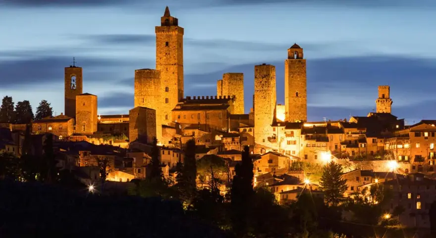 San Gimignano, una delle città più belle della Toscana, illuminata di notte con le sue iconiche torri medievali che svettano nel cielo.