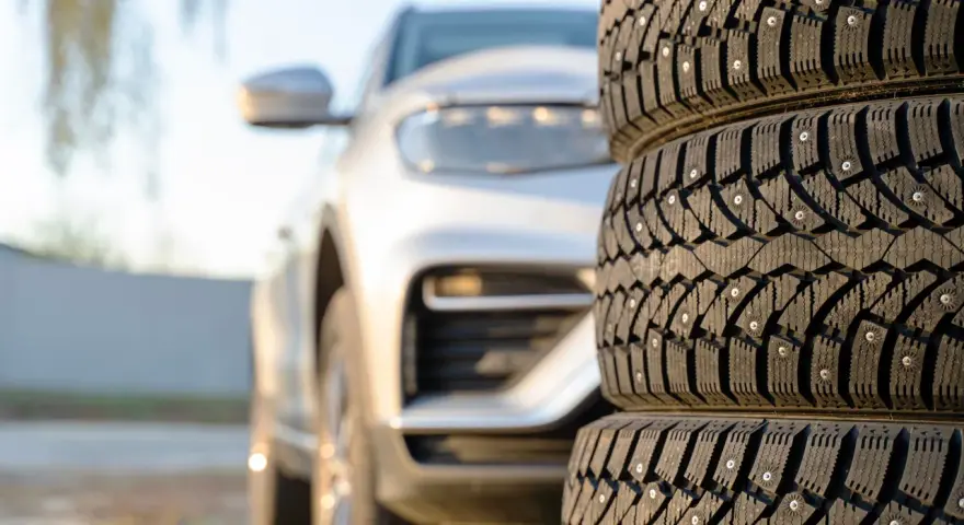 Gomme invernali con chiodi in primo piano, un'auto bianca sfocata sullo sfondo. Preparazione per l'inverno, anche se è estate.