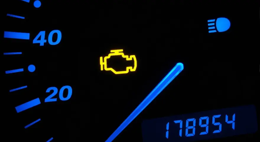 Cruscotto auto con spia motore accesa. La spia gialla a forma di motore indica un problema. Oltre, indicatori di velocità e chilometraggio.