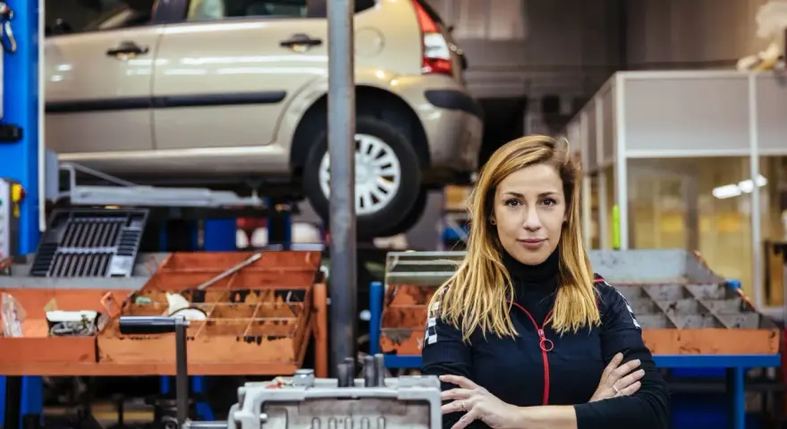 Donna in officina con auto sollevata, pronta per la manutenzione straordinaria auto.