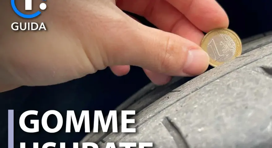 Una mano controlla l'usura di un pneumatico con una moneta da 1 euro. La tela del pneumatico è visibile, mostrando quanto sia consumata.