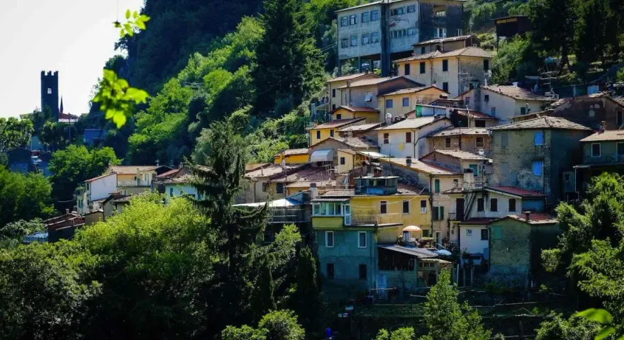 Case colorate e tetti rossi si aggrappano alla collina a Casoli di Camaiore, circondate da un verde lussureggiante.