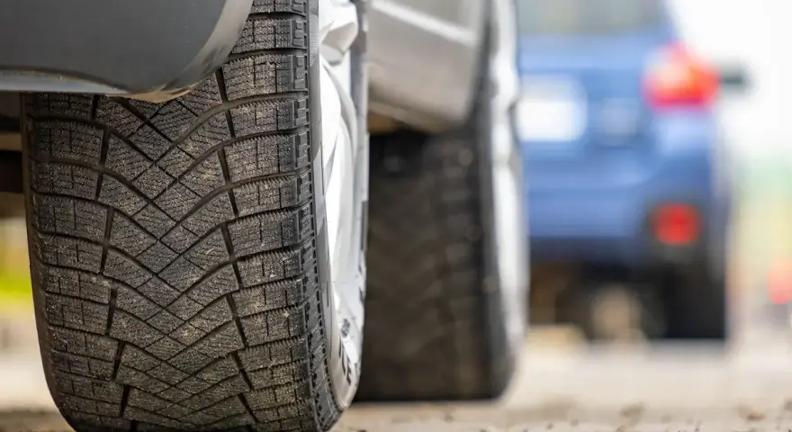 Primo piano di pneumatici invernali, con un'altra auto in lontananza. La classe rumorosità pneumatici è un fattore importante per il comfort di guida.