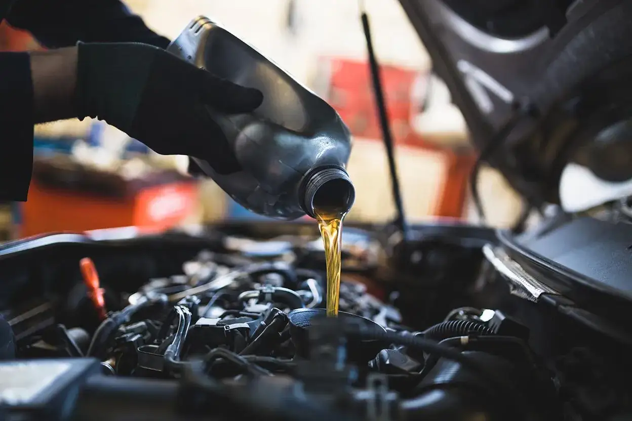 Mano con guanto versa olio motore. Per sapere cambio olio ogni quanto, consulta il manuale della tua auto.
