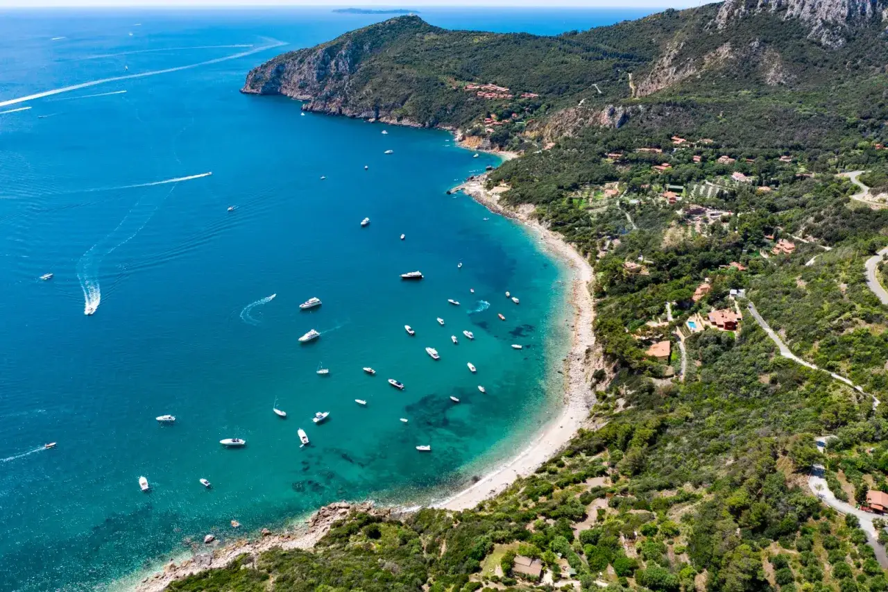 Un mare bello in Toscana, con acque cristalline e tante barche che navigano lungo la costa verdeggiante.