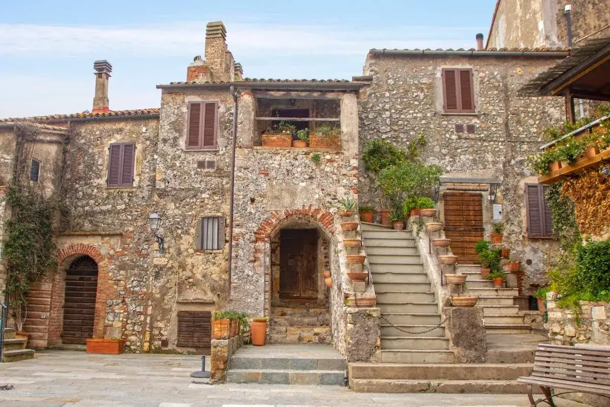 Un angolo di toscana nascosta: antiche case in pietra con scale di terracotta e piante rigogliose, un invito a scoprire i borghi autentici.