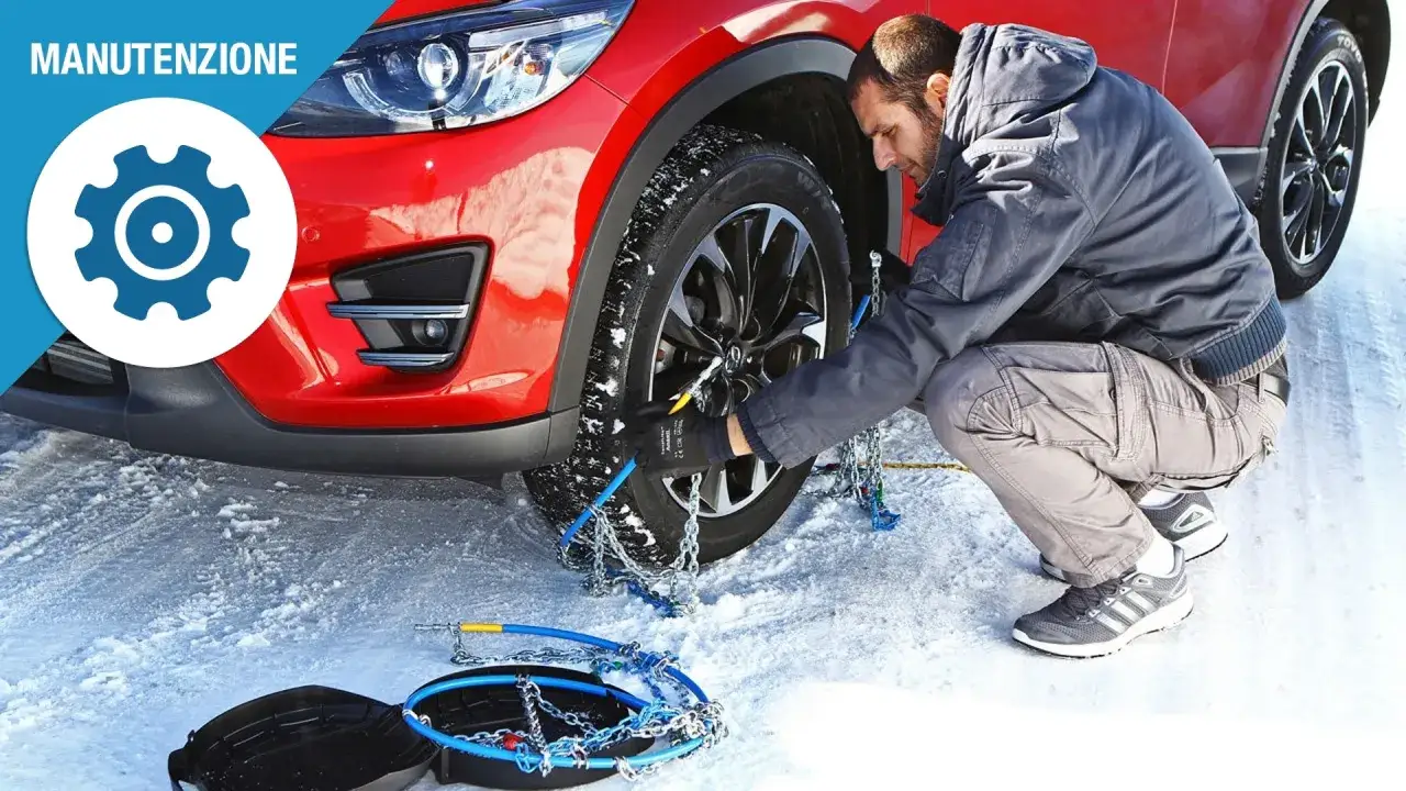 Uomo monta catene da neve su un'auto rossa in un paesaggio innevato, seguendo le indicazioni del decreto gomme per la sicurezza invernale.