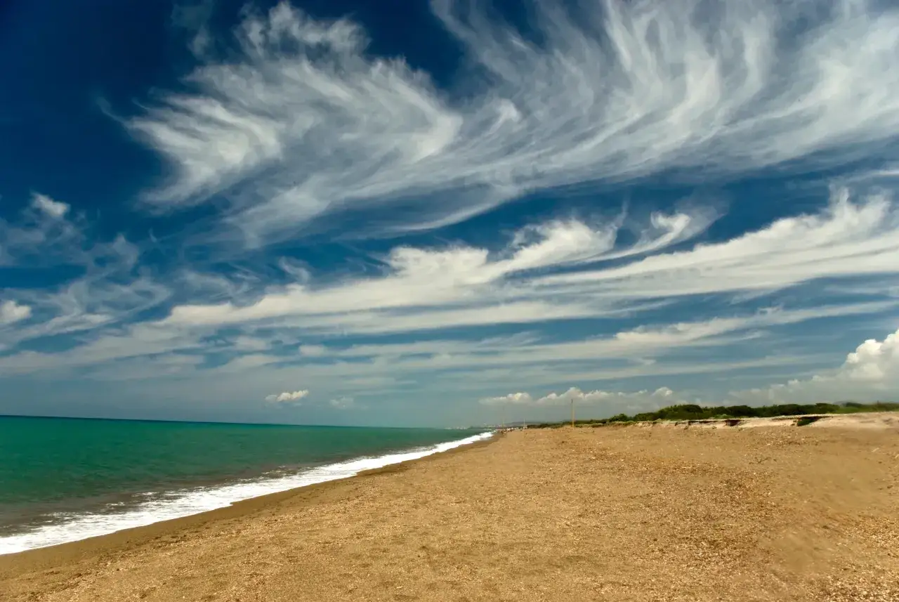 Spiaggia dorata e mare turchese al parco costiero di Rimigliano, con un cielo blu intenso solcato da nuvole bianche e vaporose.