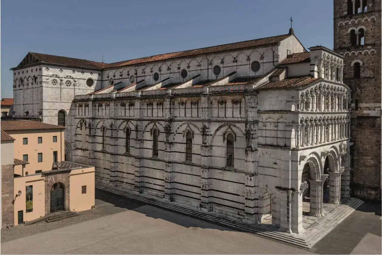La cattedrale di San Martino a Lucca, con la sua facciata in marmo bianco e nero, archi e colonne elaborate, si staglia contro il cielo azzurro.