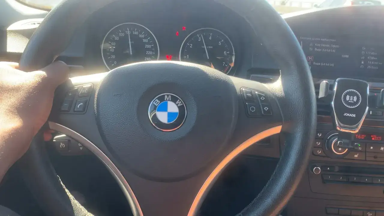 Volante BMW con cruscotto acceso, il volante trema in frenata. Si vede un telefono agganciato.
